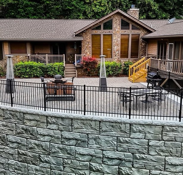 Black aluminum fence around a paver patio on top of a block retaining wall, with the house behind