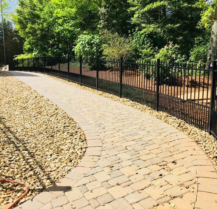 Black ornamental aluminum fence running along a curved paver walkway