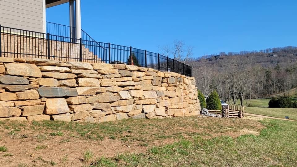 Black ornamental aluminum fence set on top of a stacked stone retaining wall with mountains behind
