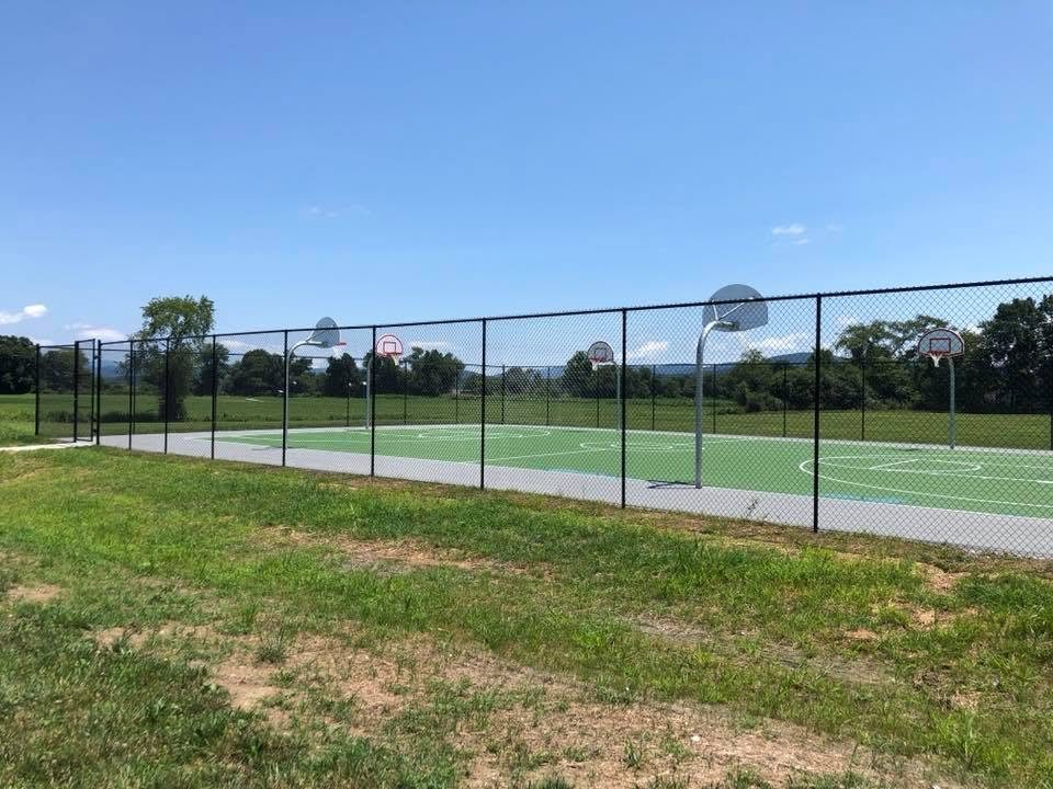 Long run of tall black chain-link fence around outdoor courts seen from the field side