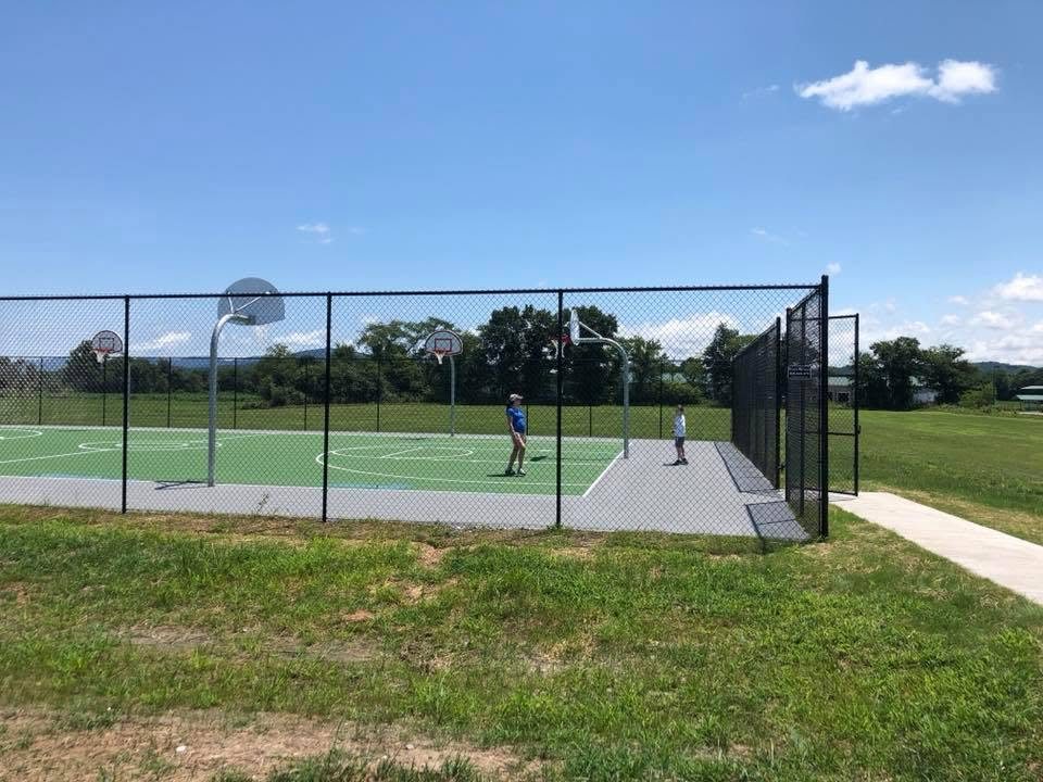 Tall black chain-link fence enclosing a basketball court complex, with a double gate at the entry