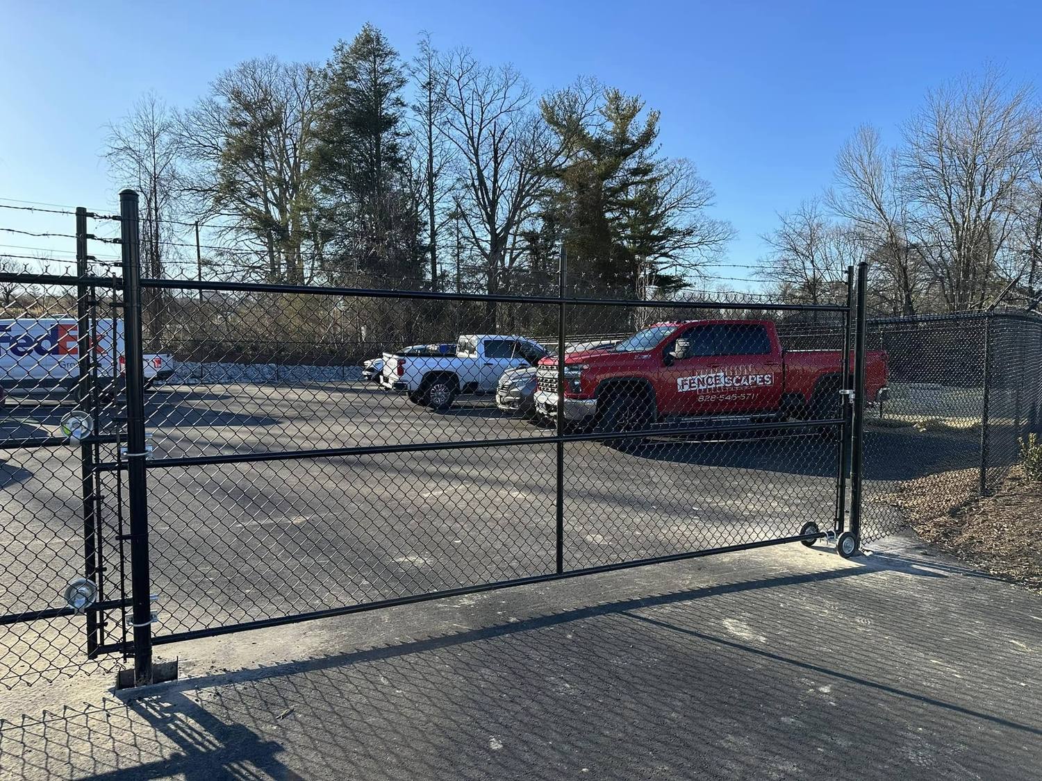 Black vinyl-coated chain-link rolling gate across a commercial parking lot entrance
