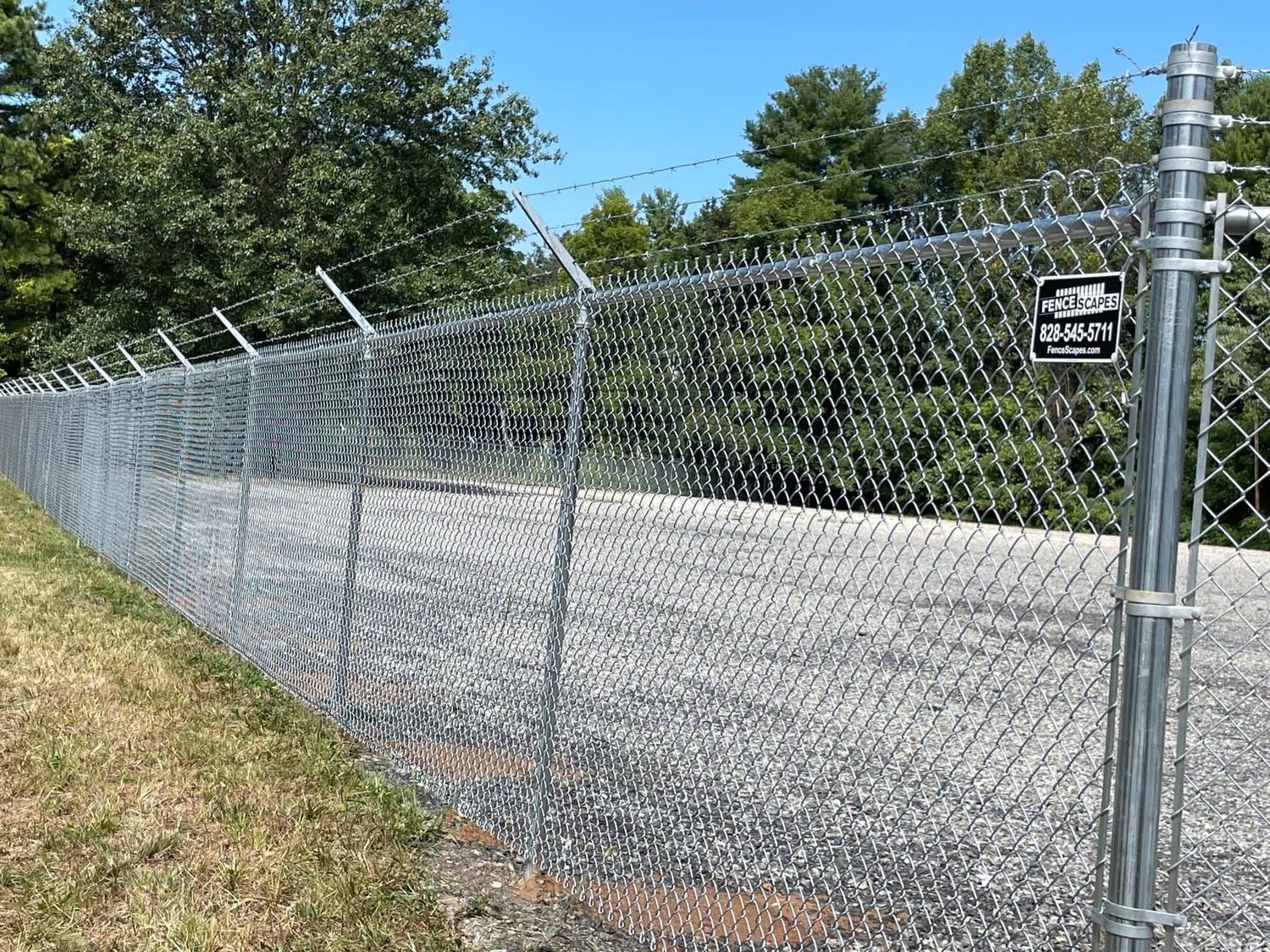 Galvanized chain-link fence with three-strand barbed arms around a paved commercial yard