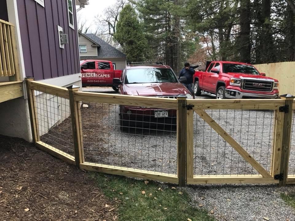 Wood-frame fence with welded wire mesh and a matching gate along a gravel drive beside a house