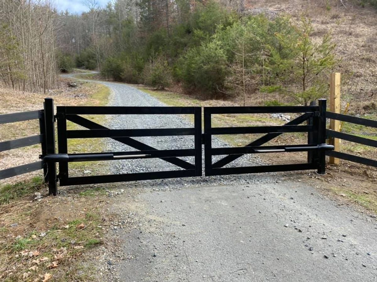 Black double farm gate across a gravel drive