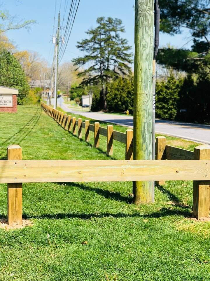 Timber post-and-rail guardrail running along a roadside yard edge