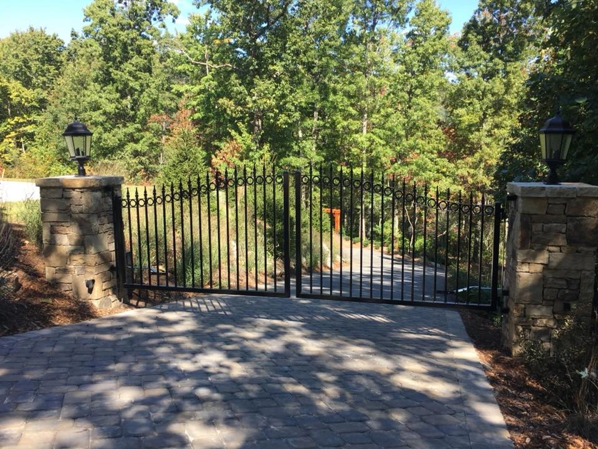 Custom black iron double swing gate between stone pillars on a paver driveway, installed by Fence Scapes near Asheville, NC