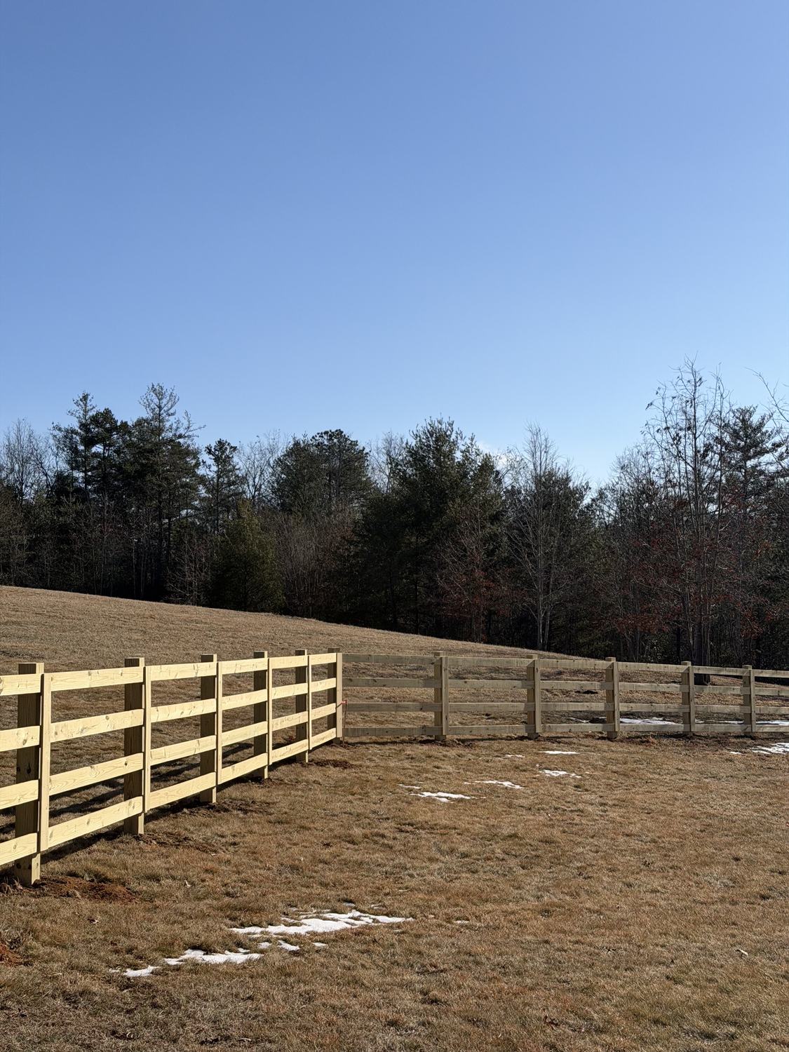 Four-rail wood fence stepping down a sloped pasture