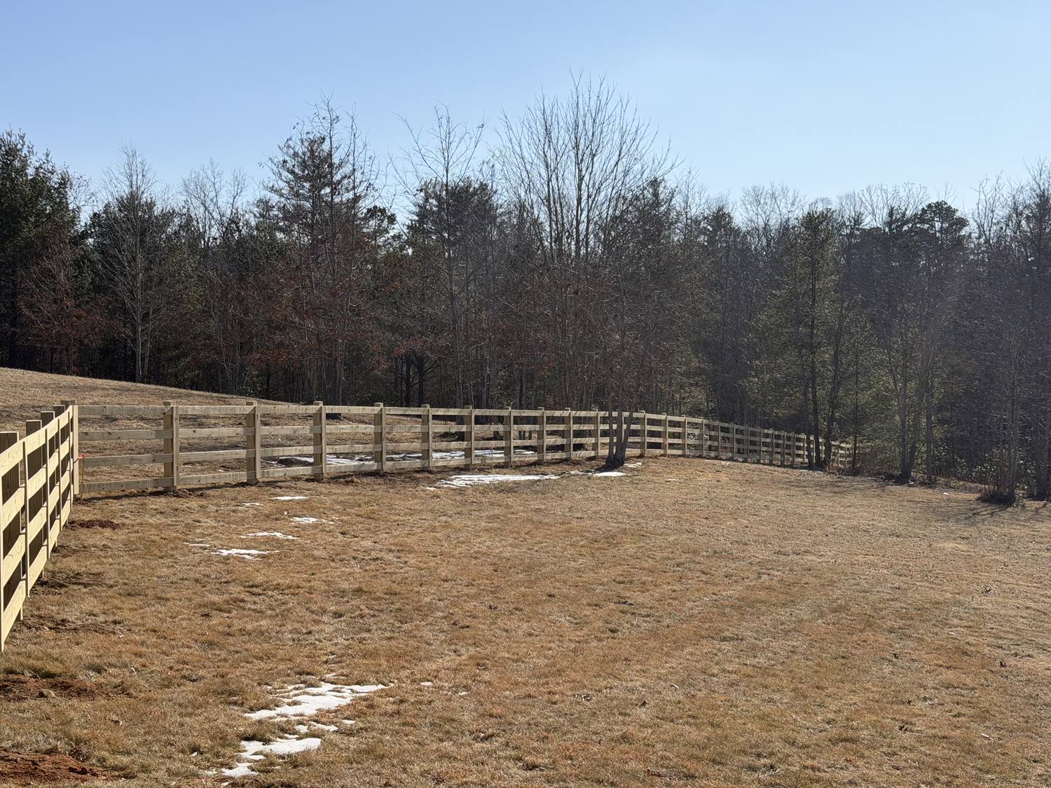 Four-rail wood fence enclosing a wide winter pasture with woods behind
