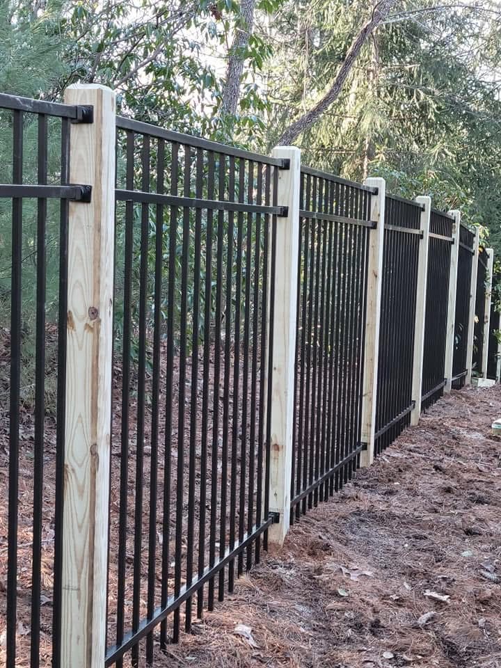 Wood-framed fence with black aluminum panels stepping down a sloped yard